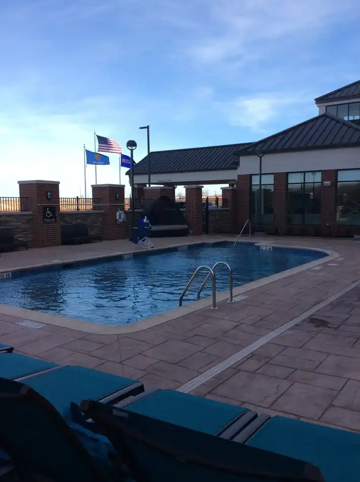 A hotel courtyard pool with an ADA pool lift, brick columns and the Oklahoma state flag flying beside the US flag