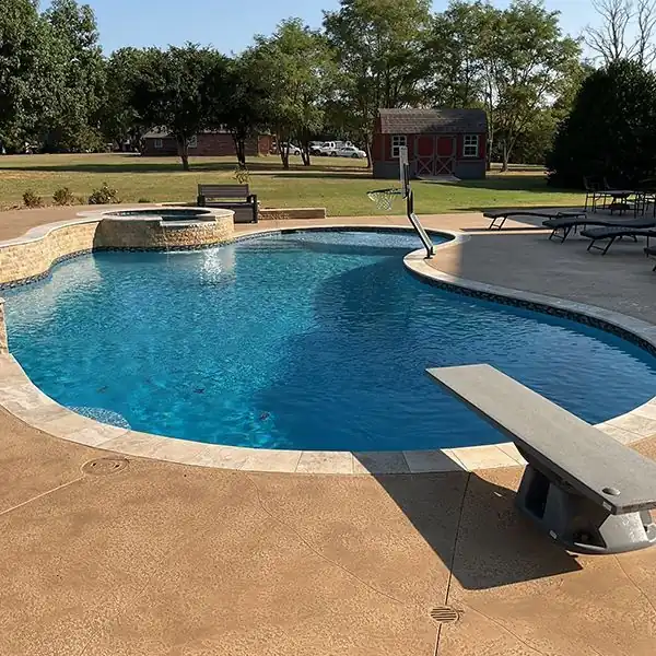 A backyard pool with a diving board and a tan Sundek resurfaced deck beside a red barn shed