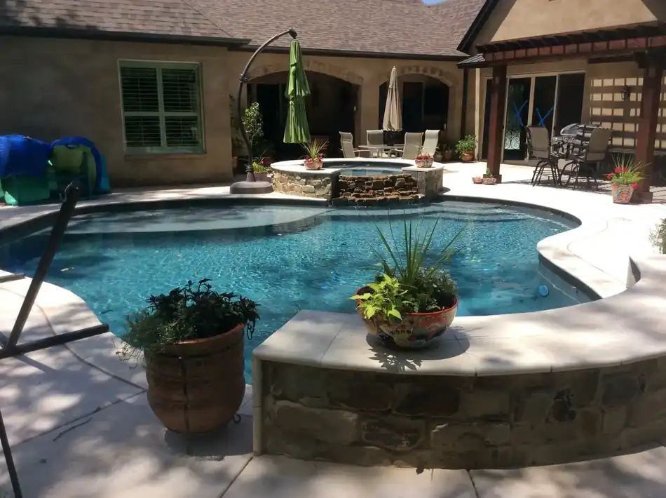 A freeform pool with a raised spa fed by a stacked stone waterfall, beside a stucco home