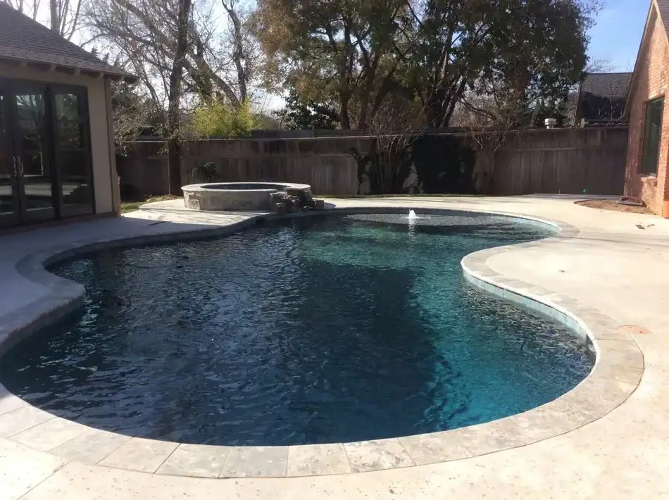 A freeform pool with a raised round stone spa with a spillway, travertine coping and a brick home behind