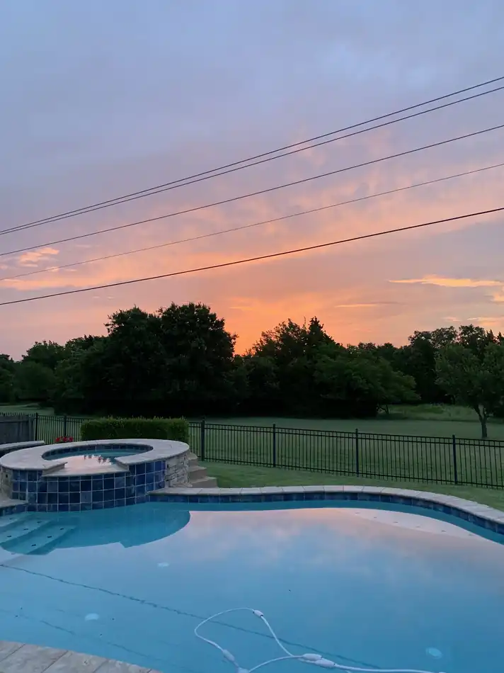 A raised blue tile spa with spillway steps beside a rectangular pool under an orange Oklahoma sunset