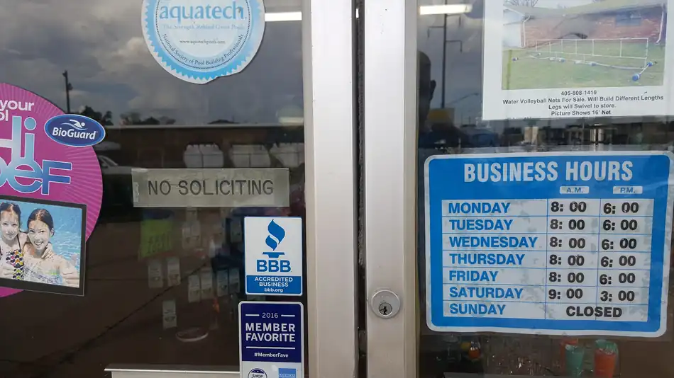 The front door of the Cardinal Pools store on NW 10th, carrying the Aquatech pool builders seal, a BioGuard decal, a BBB Accredited Business decal and the printed business hours